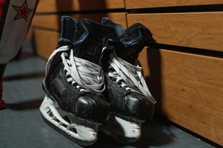 a pair of hockey skates leaning against a wall, in an arena pit, photograph taken in 2 0 2 0, fan favorite, black