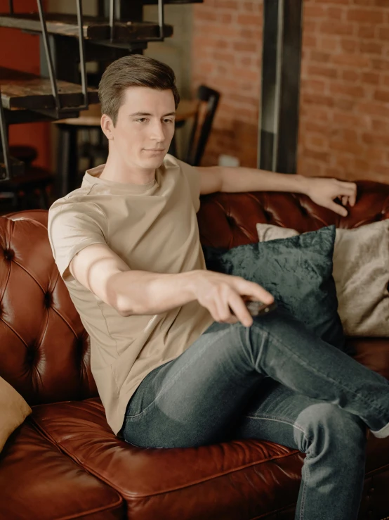 a man sitting on top of a brown couch, wearing tight shirt, connor hibbs, hand on hip, background image