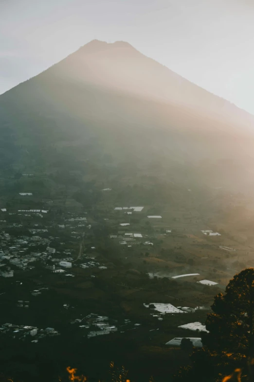 a person standing on top of a hill with a mountain in the background, trending on unsplash, sumatraism, mexico city, volcano texture, background image, realistic photo of a town