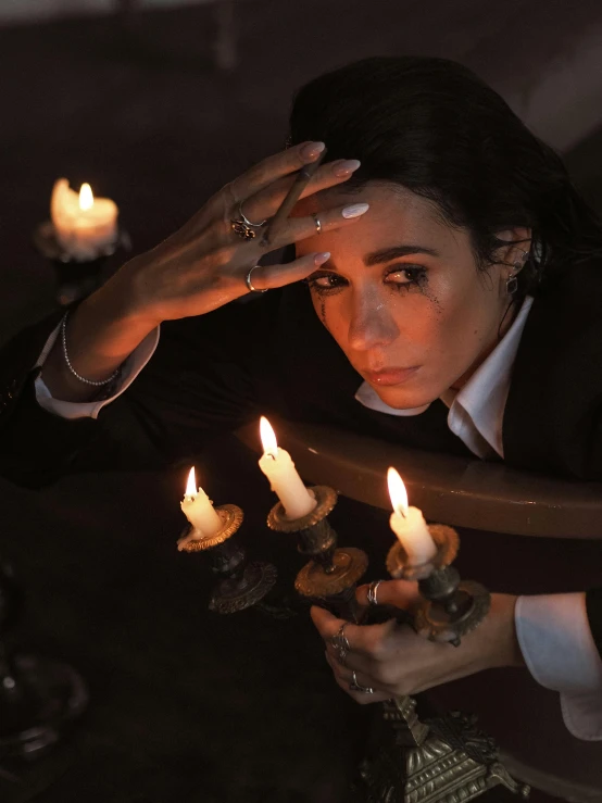 a woman lighting candles in a dark room, an album cover, inspired by Marina Abramović, trending on pexels, magical realism, winona ryder, sad man, maya ali as a mage, ( ( theatrical ) )