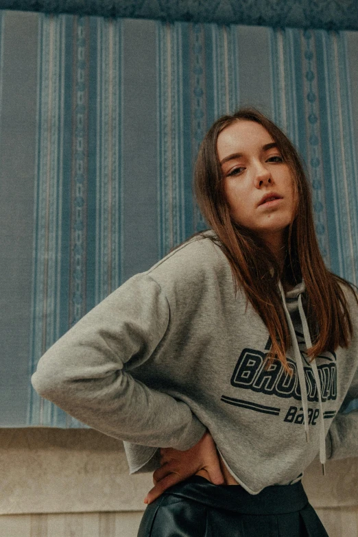 a woman leaning against a wall with her hands on her hips, an album cover, inspired by Elsa Bleda, unsplash contest winner, wearing a grey hooded sweatshirt, sydney sweeney, sitting in her room, bashful expression