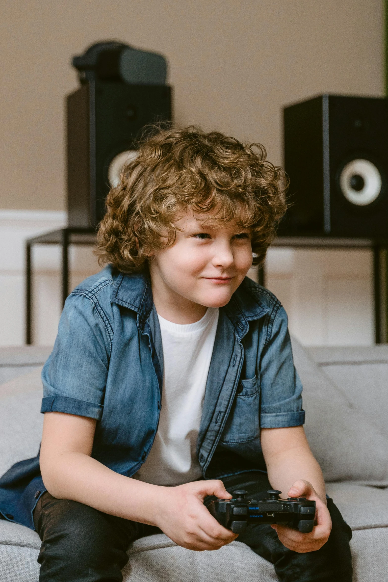 a young boy sitting on a couch holding a video game controller, an album cover, by Everett Warner, trending on pexels, happening, curly brown hair, tannoy, denim, avatar image