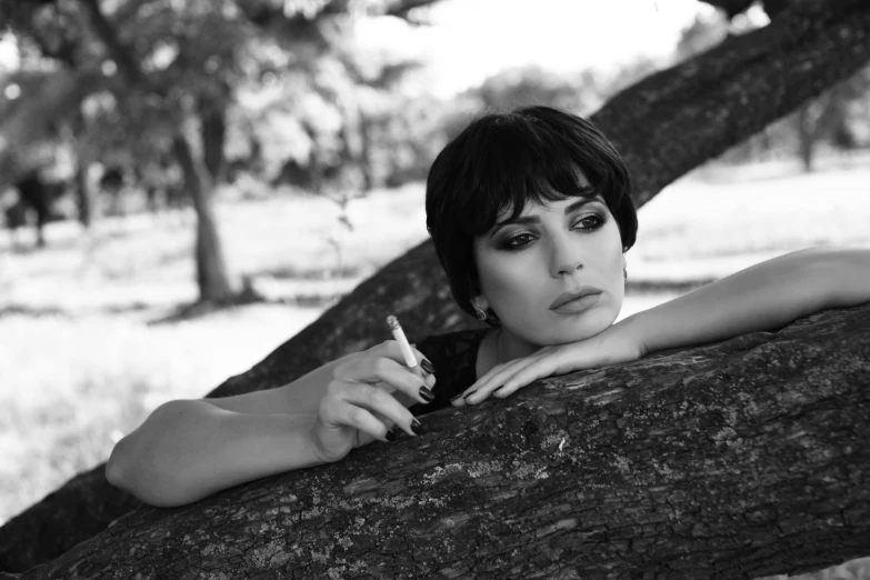 a black and white photo of a woman leaning against a tree, a black and white photo, pixabay, cigarettes, black short hair, young arab monica bellucci, pixie cut