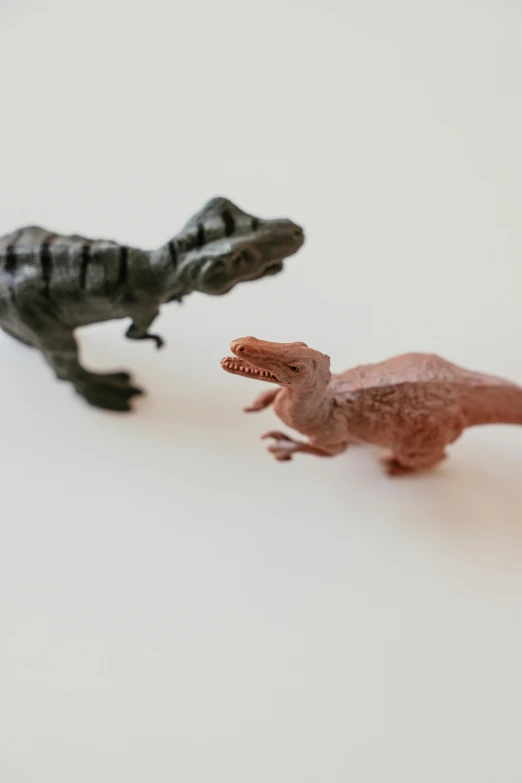 a couple of toy dinosaurs standing next to each other, by Adam Rex, trending on unsplash, made out of plastic, half turned around, hand, 1979