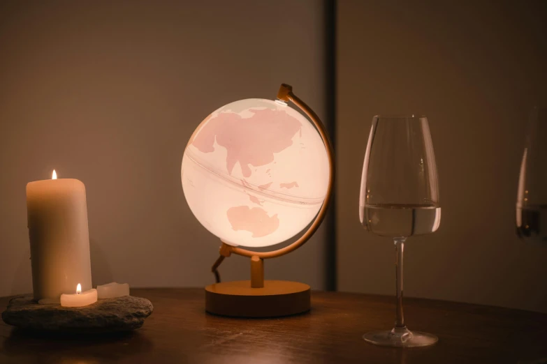 a lighted globe sitting on top of a table next to a glass of wine, light pink mist, mood light, glowing epicentre, marbling effect