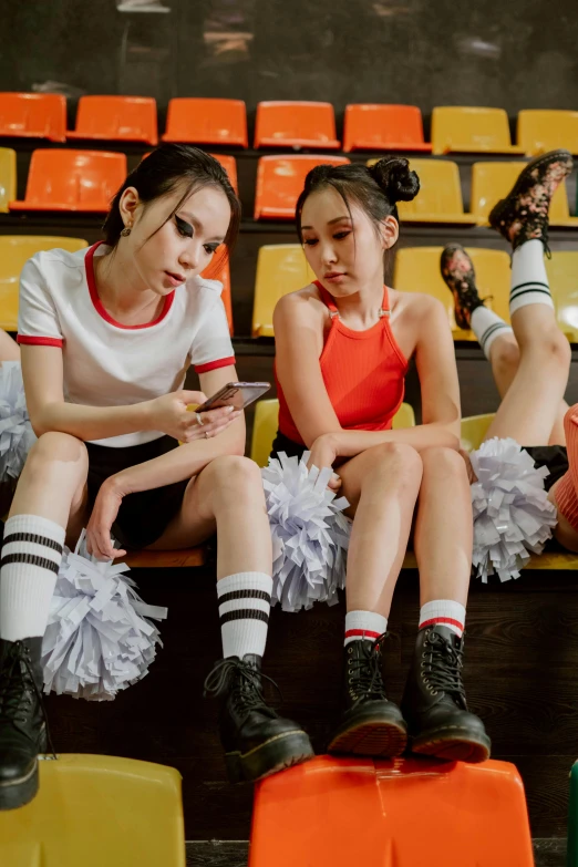 a group of young women sitting next to each other, a cartoon, inspired by Nan Goldin, trending on pexels, a teenage girl cheerleader, set on singaporean aesthetic, professional sports style, medium shot of two characters