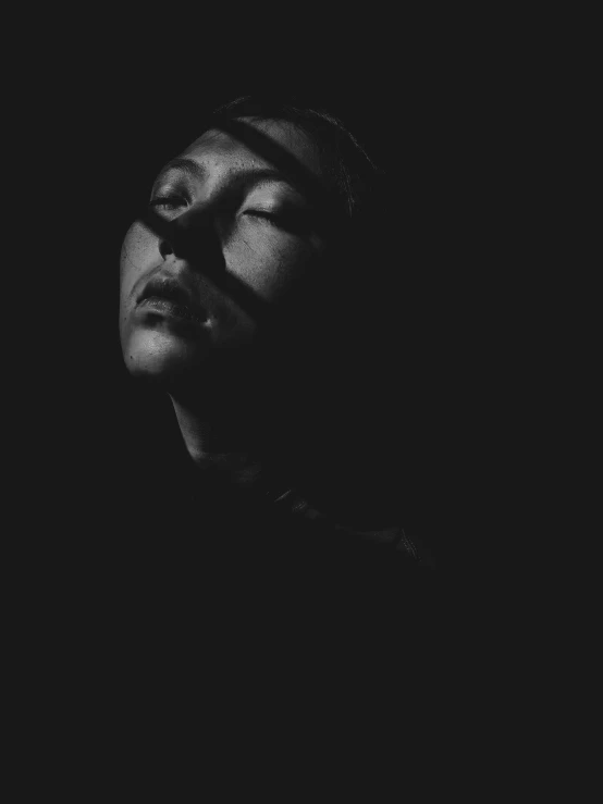 a man with his eyes closed in the dark, a black and white photo, by Emma Andijewska, unsplash, arca album cover, portrait sophie mudd, she is laying on her back, shaded face