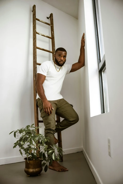 a man leaning on a ladder next to a potted plant, inspired by Paul Georges, trending on pexels, handsome hip hop young black man, square, standing in corner of room, jaylen brown