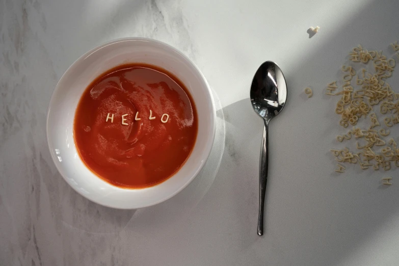 a bowl of tomato soup next to a spoon, inspired by Heinz Edelman, unsplash, hyperrealism, hidden message, hello, embossed, on grey background