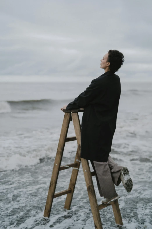 a man standing on top of a wooden ladder, an album cover, unsplash, romanticism, she is wearing a wet coat, on the coast, thoughtful pose, asian male