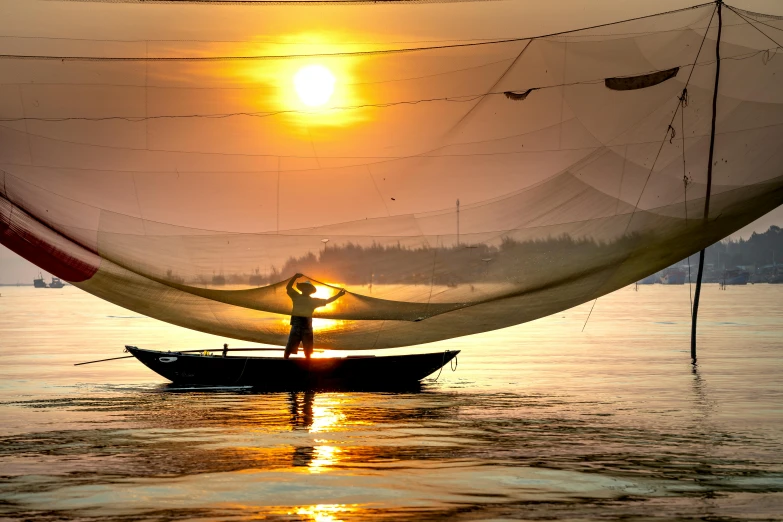 a man standing on top of a boat in the water, inspired by Steve McCurry, pexels contest winner, solar sails, vietnamese woman, warm glow, netting