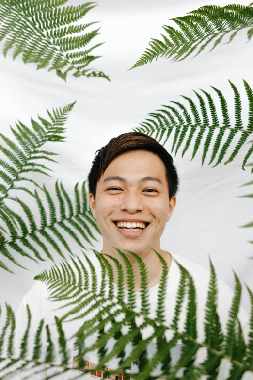 a man standing in front of a bunch of green leaves, inspired by Reuben Tam, pexels contest winner, sumatraism, smiling male, in front of white back drop, fern, asian face