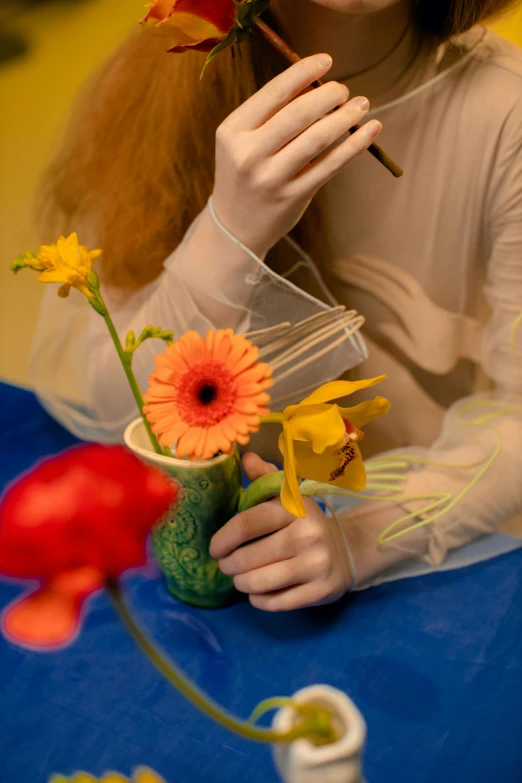 a woman sitting at a table with a flower in her hand, an album cover, unsplash, hyperrealism, sadie sink, hans bellmer and wlop, primary colours, detail shot