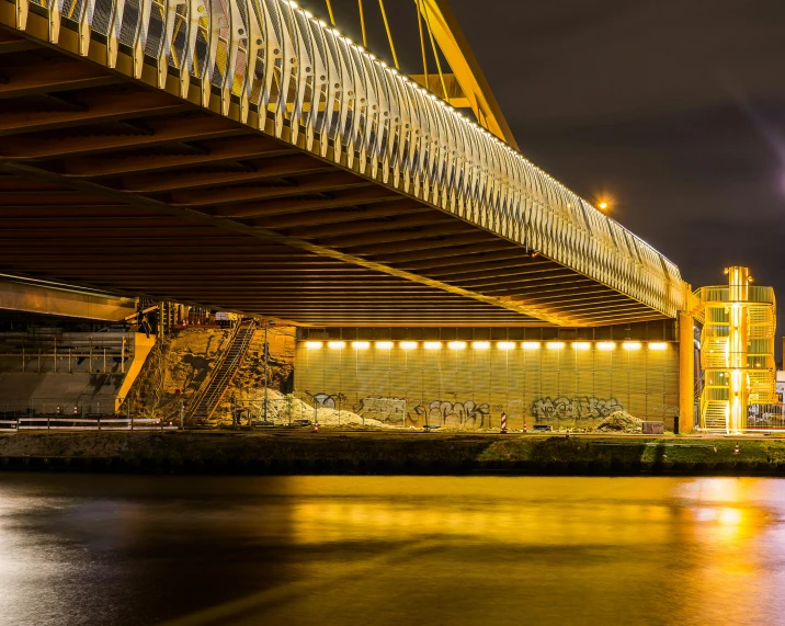 a bridge over a body of water at night, by Adam Marczyński, pexels contest winner, graffiti, brown, construction, liquid gold, panoramic shot