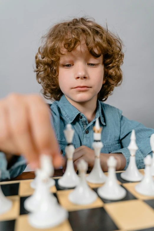 a young boy playing a game of chess, a colorized photo, by Daniel Seghers, trending on unsplash, on grey background, curls on top, thumbnail, miniatures