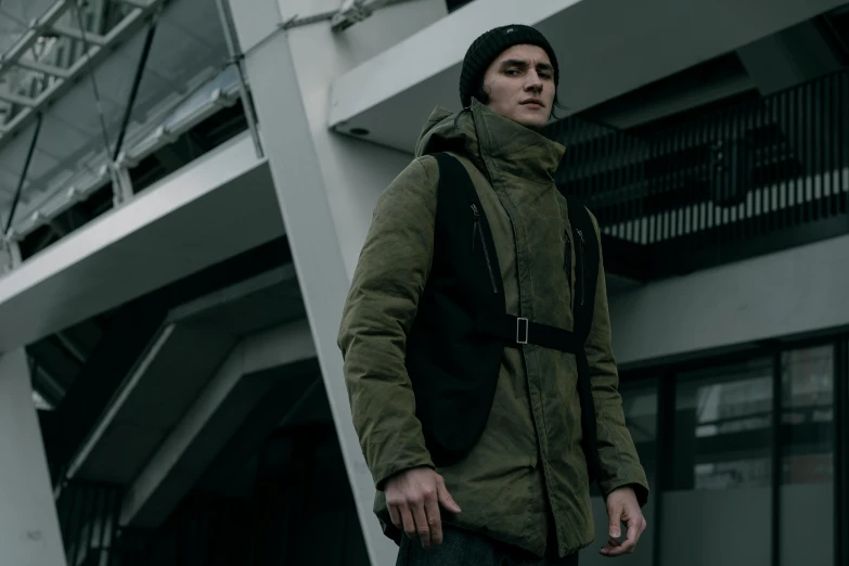 a man standing on a skateboard in front of a building, inspired by Kanō Hōgai, unsplash, bauhaus, model wears a puffer jacket, dark green tones, worksafe. cinematic, front