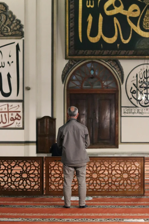 a man standing in front of a wall with arabic calligraphy, hurufiyya, trump praying in mosque, filmstill, cairo, multiple stories