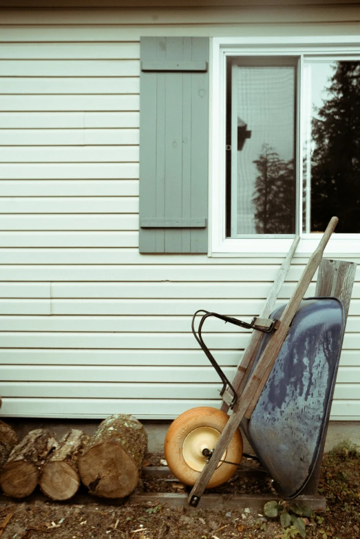 a wheelbarrow and a pile of logs in front of a house, unsplash, photorealism, cyan shutters on windows, white plank siding, close - up photograph, late summer evening