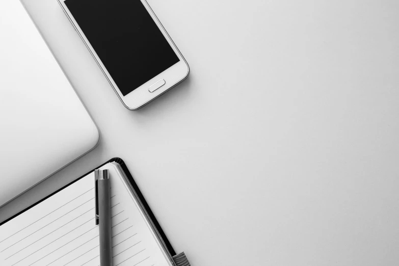 a white laptop computer sitting on top of a desk next to a cell phone, a black and white photo, trending on pexels, minimalism, pen, phone wallpaper, background image, product introduction photo