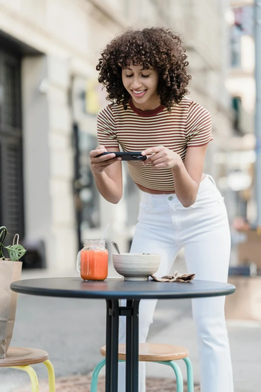 a woman sitting at a table looking at her phone, trending on pexels, happening, standing in a city center, wearing a cropped top, playful composition, product introduction photo