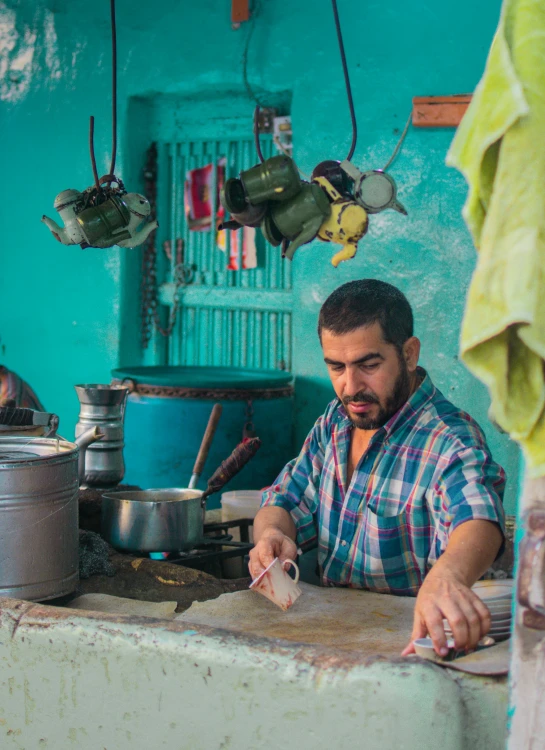 a man sitting at a counter in a kitchen, pexels contest winner, cuban setting, square, working in the forge, a colorful