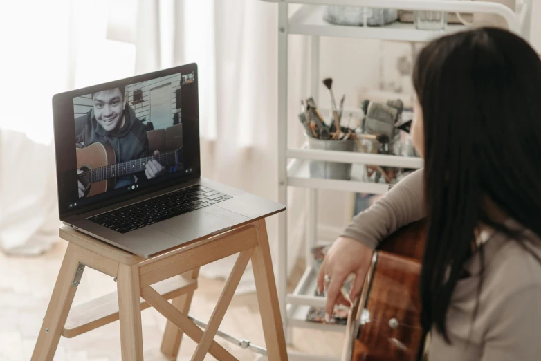 a woman sitting in front of a laptop computer, a picture, by Julia Pishtar, trending on pexels, holding a guitar, teaching, casey cooke, long distance photo