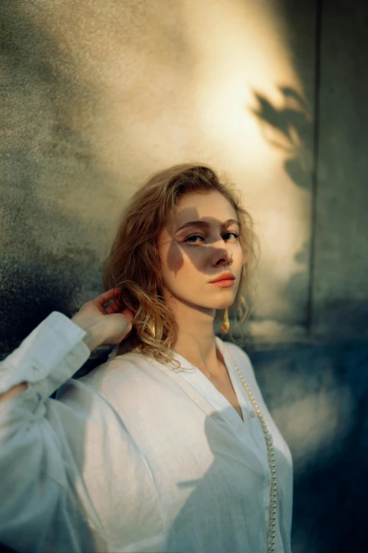 a woman in a white shirt leaning against a wall, an album cover, inspired by Elsa Bleda, trending on pexels, renaissance, sophia lillis, evening sunlight, portrait image, bleached