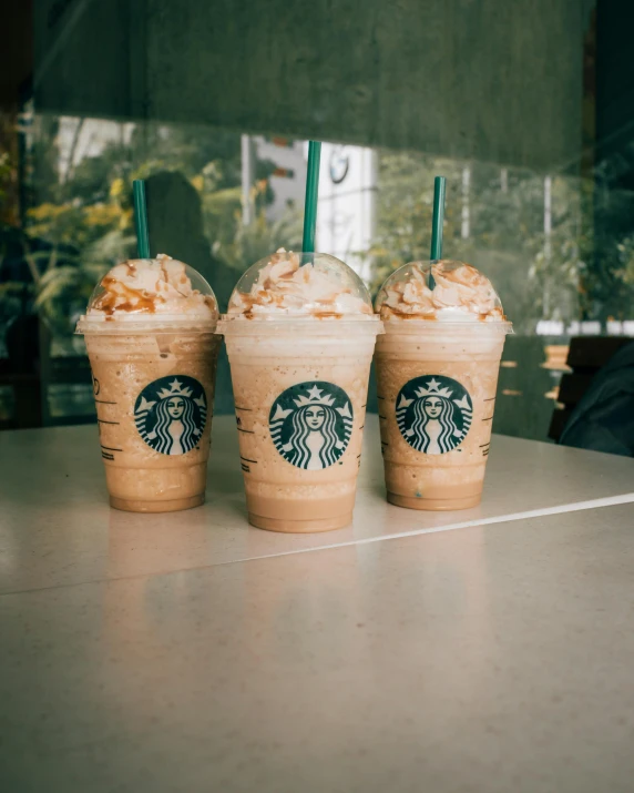 three cups of coffee sitting on top of a table, a colorized photo, by Elsa Bleda, trending on unsplash, renaissance, thanos as a starbucks barista, milkshake, lesbians, brown and white color scheme