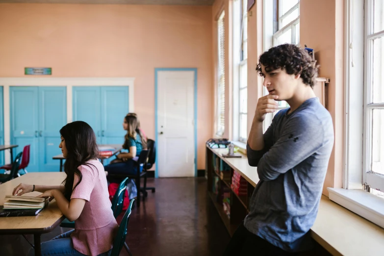 a couple of people sitting at a table in a room, trending on pexels, ashcan school, teenage boy, standing in class, contemplation, person in foreground