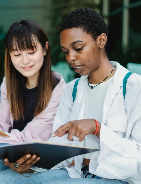 a couple of women sitting next to each other on a bench, trending on pexels, academic art, standing in class, textbooks, diverse colors, official screenshot