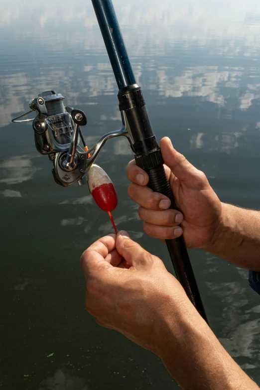 a man holding a fishing rod next to a lake, in the middle of a lake, up-close, mechanised, hanging