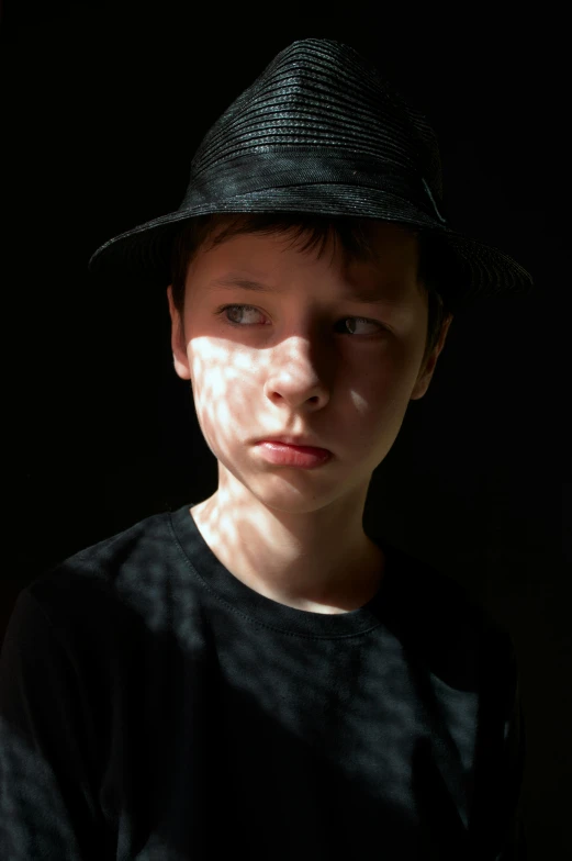 a close up of a person wearing a hat, by Sven Erixson, pexels, hyperrealism, light over boy, dramatic backlight, looking serious, teen boy