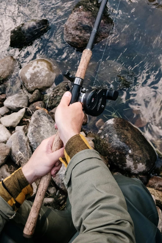 a man holding a fishing rod next to a body of water, a high angle shot, rapids, shot with sony alpha, black