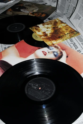 a couple of vinyl records sitting on top of a newspaper, an album cover, inspired by Nan Goldin, synthetism, madonna, uncropped, show from below, low quality photo