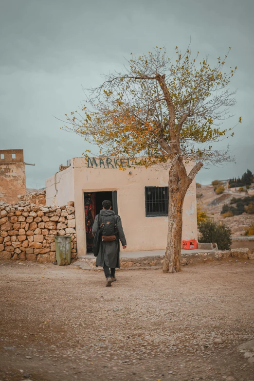 a person walking down a dirt road in front of a building, les nabis, cave town, fall season, mad max inspired, olive tree