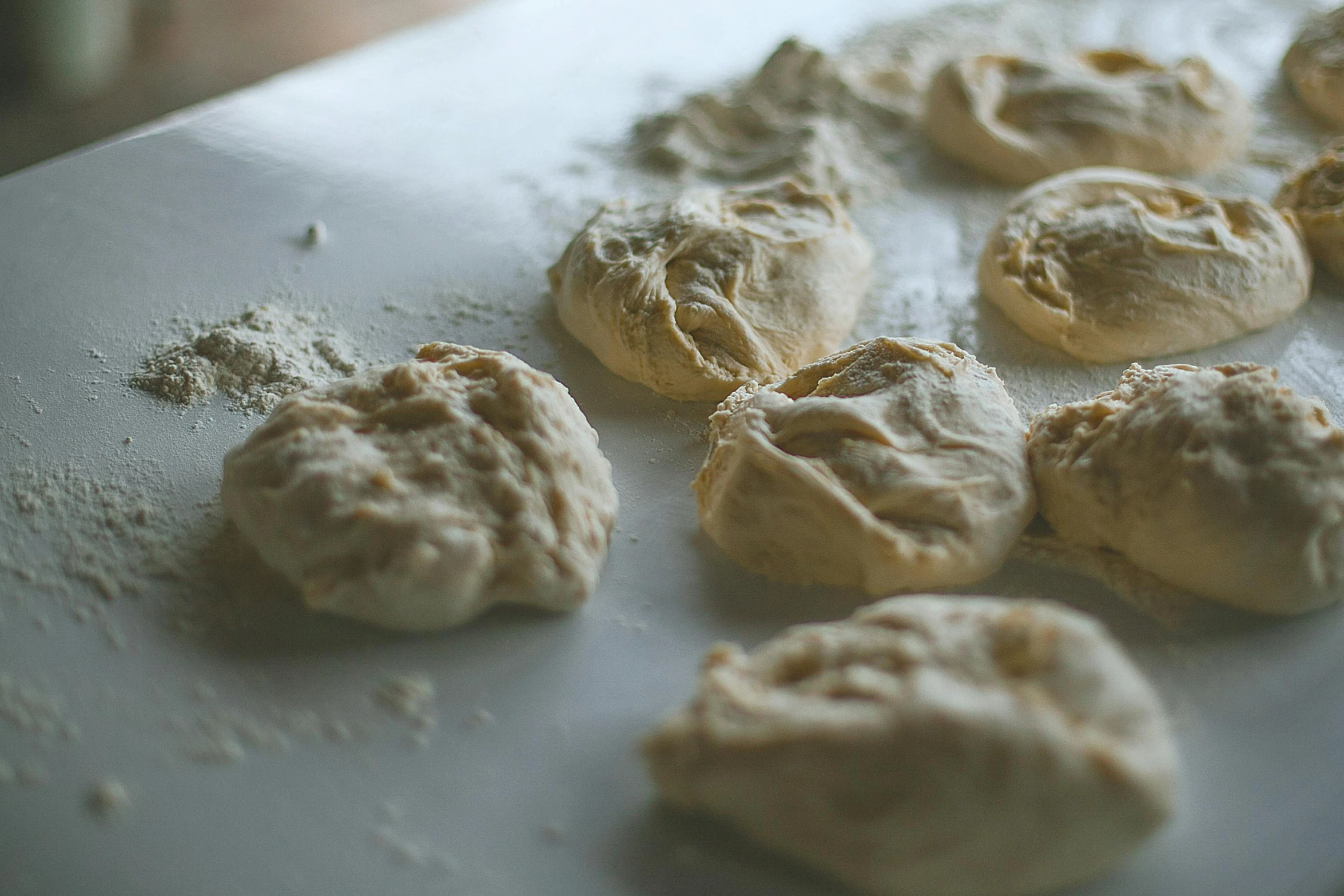 a white plate topped with doughnuts on top of a table, by Sylvia Wishart, unsplash, process art, dumplings on a plate, flour dust, mead, slightly blurry