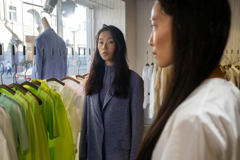 a woman standing in front of a rack of clothes, inspired by Kim Tschang Yeul, pexels contest winner, gutai group, wearing hi vis clothing, wearing a linen shirt, two models in the frame, looking across the shoulder