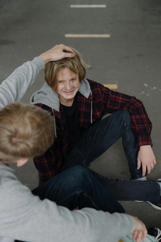 two young men sitting on the ground with skateboards, trending on pexels, incoherents, caring fatherly wide forehead, blond boy, greeting hand on head, getting ready to fight