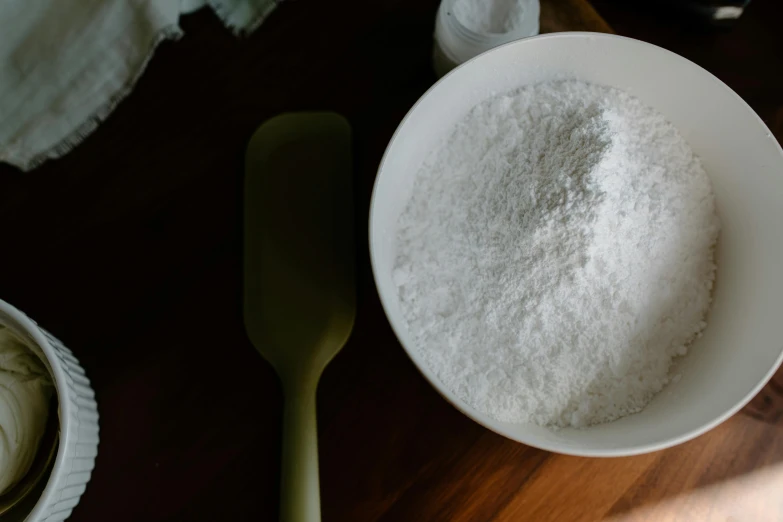 a white bowl sitting on top of a wooden table, covered in white flour, tools, slightly pixelated, thumbnail