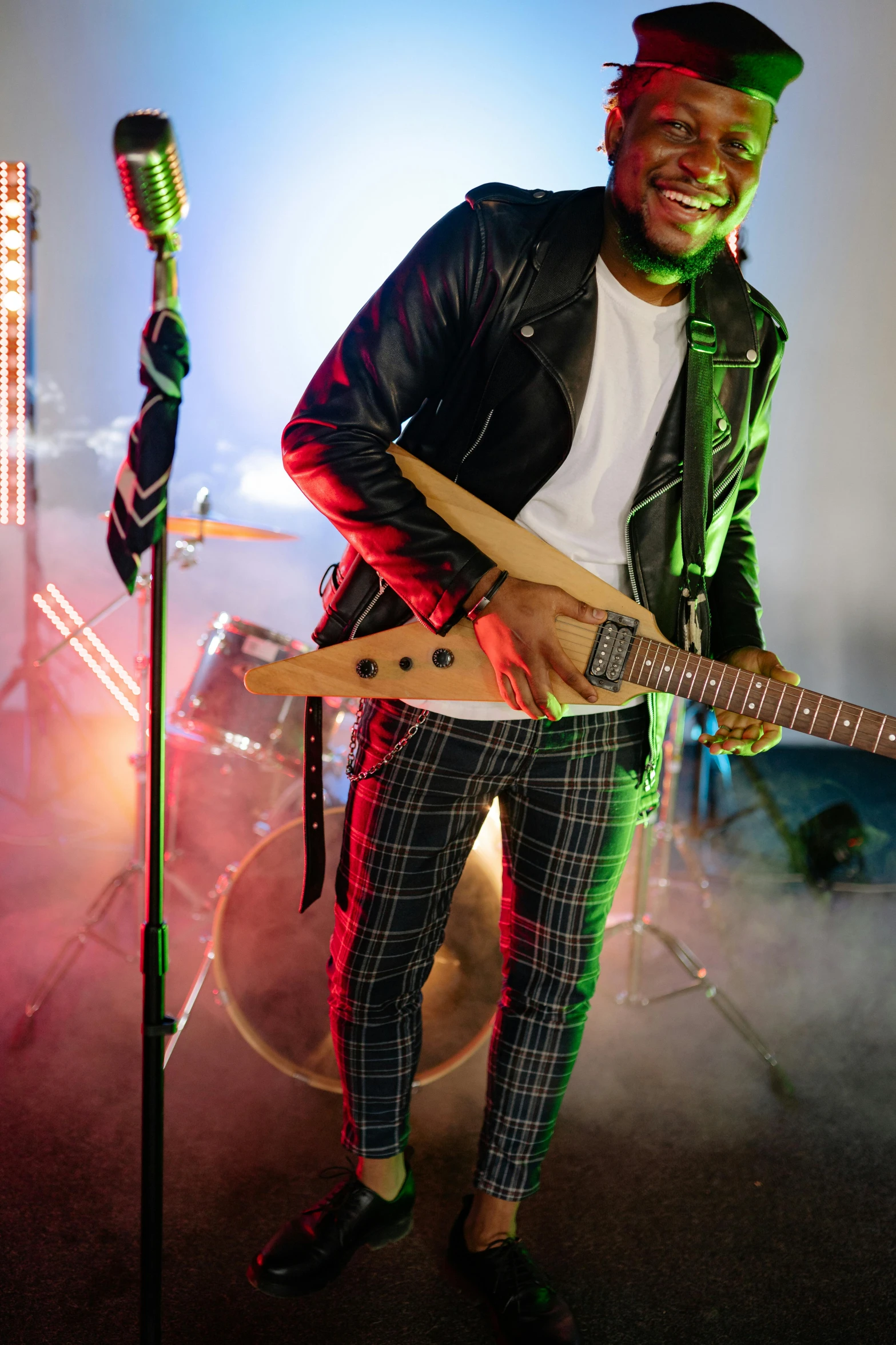 a man standing in front of a microphone holding a guitar, trending on pexels, wearing studded leather, vibrant lights, riyahd cassiem, cinematic outfit photo