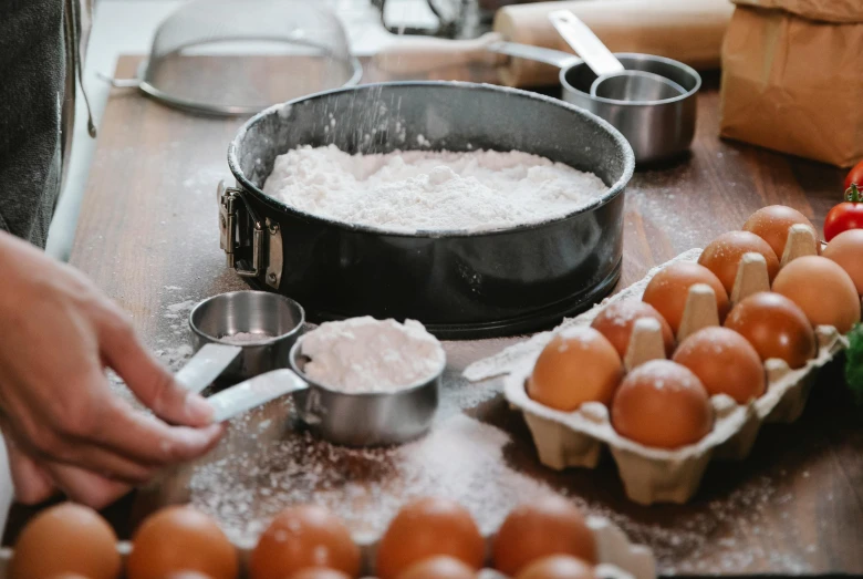 a person preparing food on a wooden table, a still life, trending on pexels, covered in white flour, pots and pans, eggs, cake