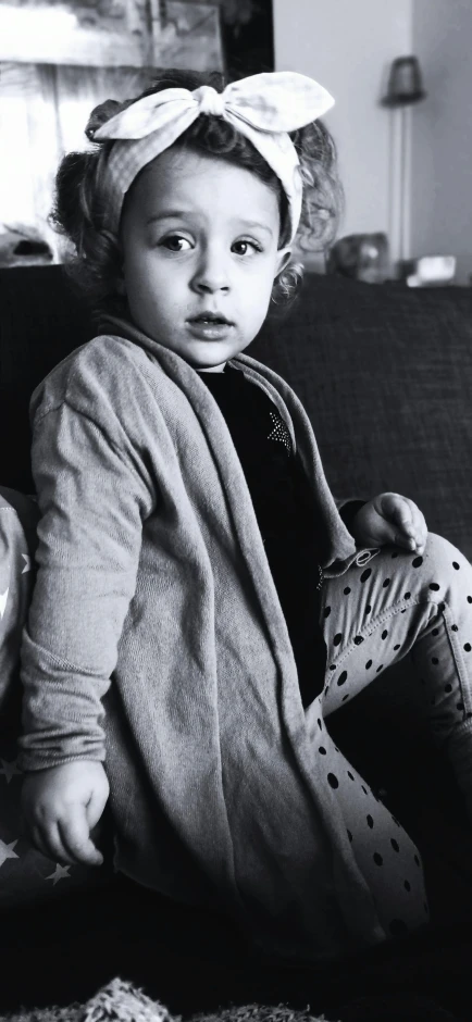 a black and white photo of a little girl sitting on a couch, by Lucia Peka, pexels contest winner, photorealism, cardigan, toddler, 15081959 21121991 01012000 4k, wearing pajamas