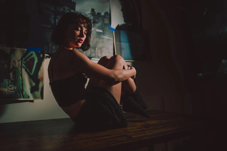 a woman sitting on top of a wooden table, a portrait, inspired by Elsa Bleda, unsplash, dimly lit dive bar, infp young woman, in her room, leg and thigh shot