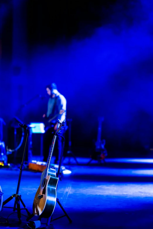 a man standing on top of a stage next to a guitar, pexels, blue blurred, panoramic, college, theatrical lighting