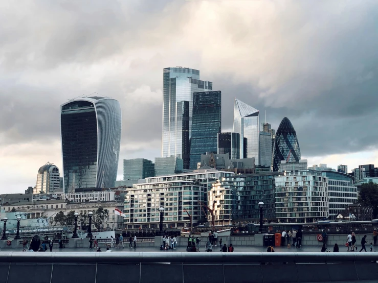 a group of people walking across a bridge next to tall buildings, an album cover, inspired by Thomas Struth, pexels contest winner, hyperrealism, river thames, photo of futuristic cityscape, a small, panoramic