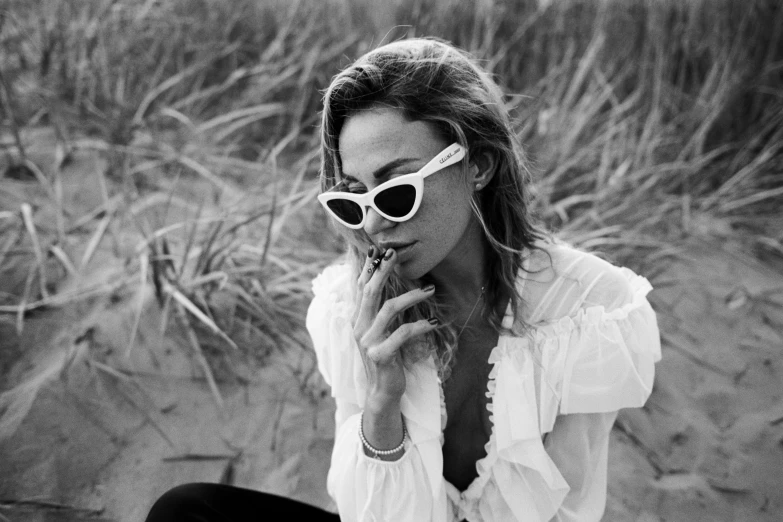 a black and white photo of a woman smoking a cigarette, by Emma Andijewska, margot robbie on the beach, designer sunglasses, wearing a white blouse, medium format. soft light