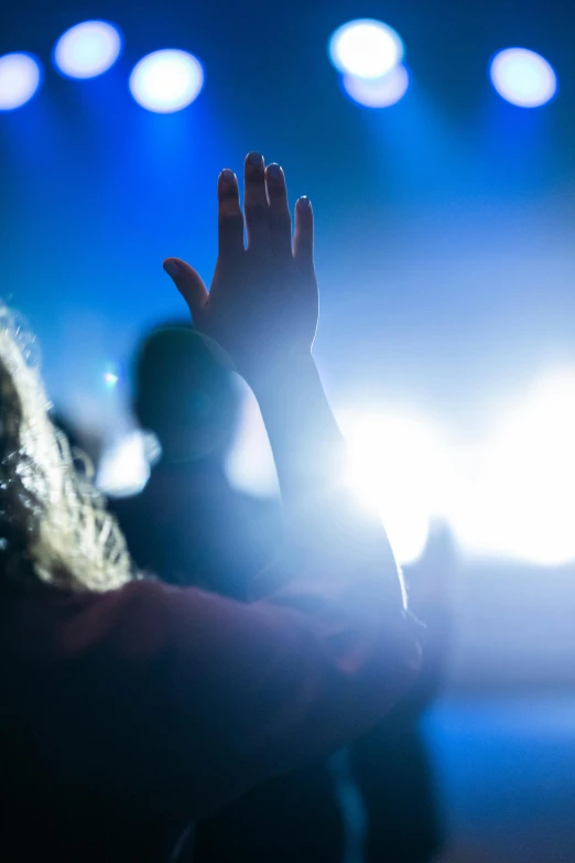 a person raising their hand at a concert, by Dan Content, pexels, doing a prayer, getty images, promo image, backlighted