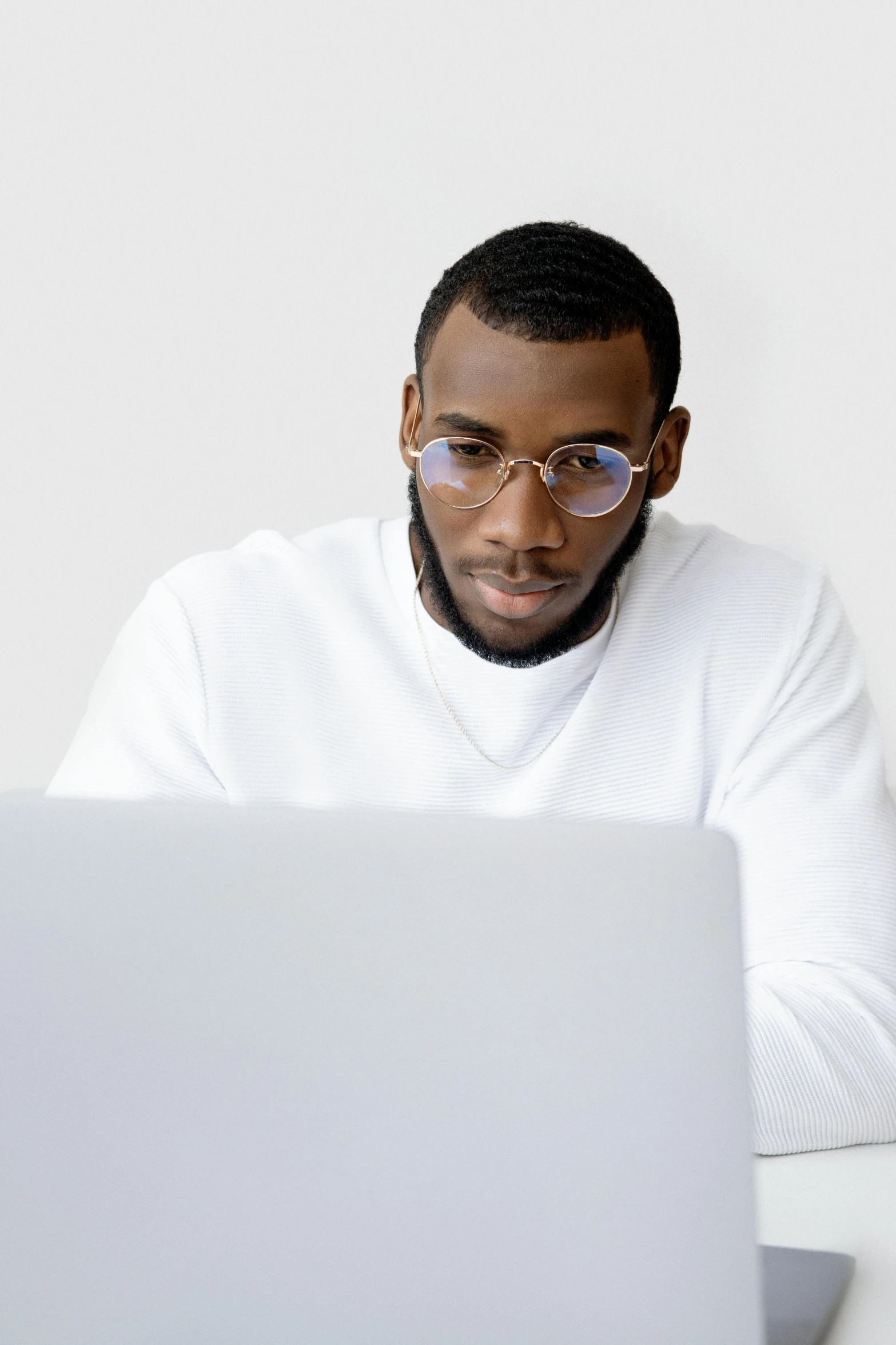 a man sitting in front of a laptop computer, by Carey Morris, trending on pexels, renaissance, plain background, ( ( dark skin ) ), white reading glasses, official screenshot