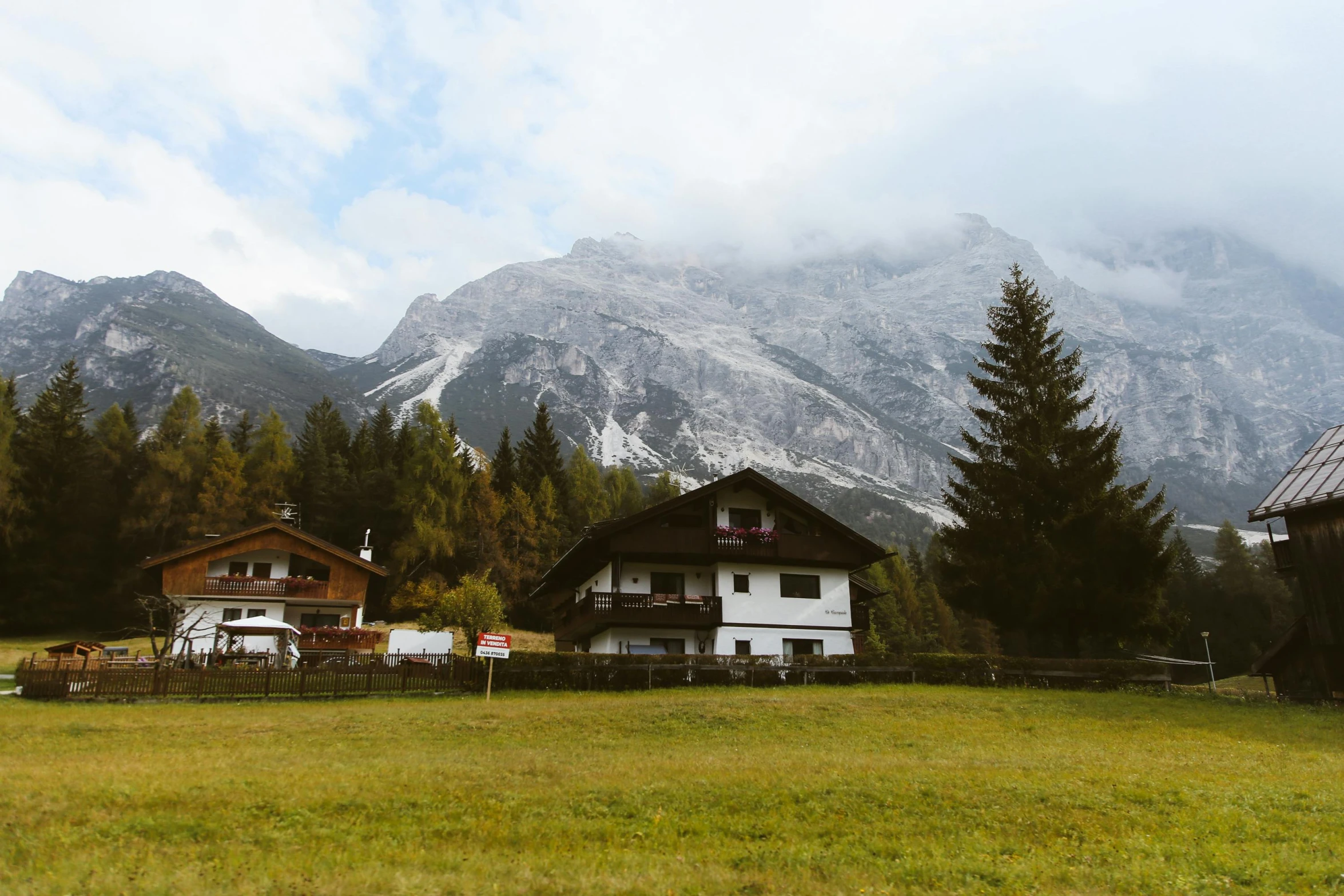 a couple of houses sitting on top of a lush green field, by Sebastian Spreng, pexels contest winner, snow capped mountains, wes anderson style, white marble buildings, 70s photo