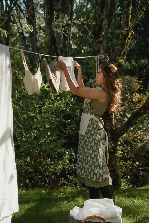 a woman hanging clothes on a clothes line, organic dress, muted green, slide show, apron